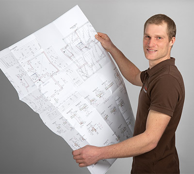 Lukas Gloeckler Portrait mit einem Bauplan in der Hand